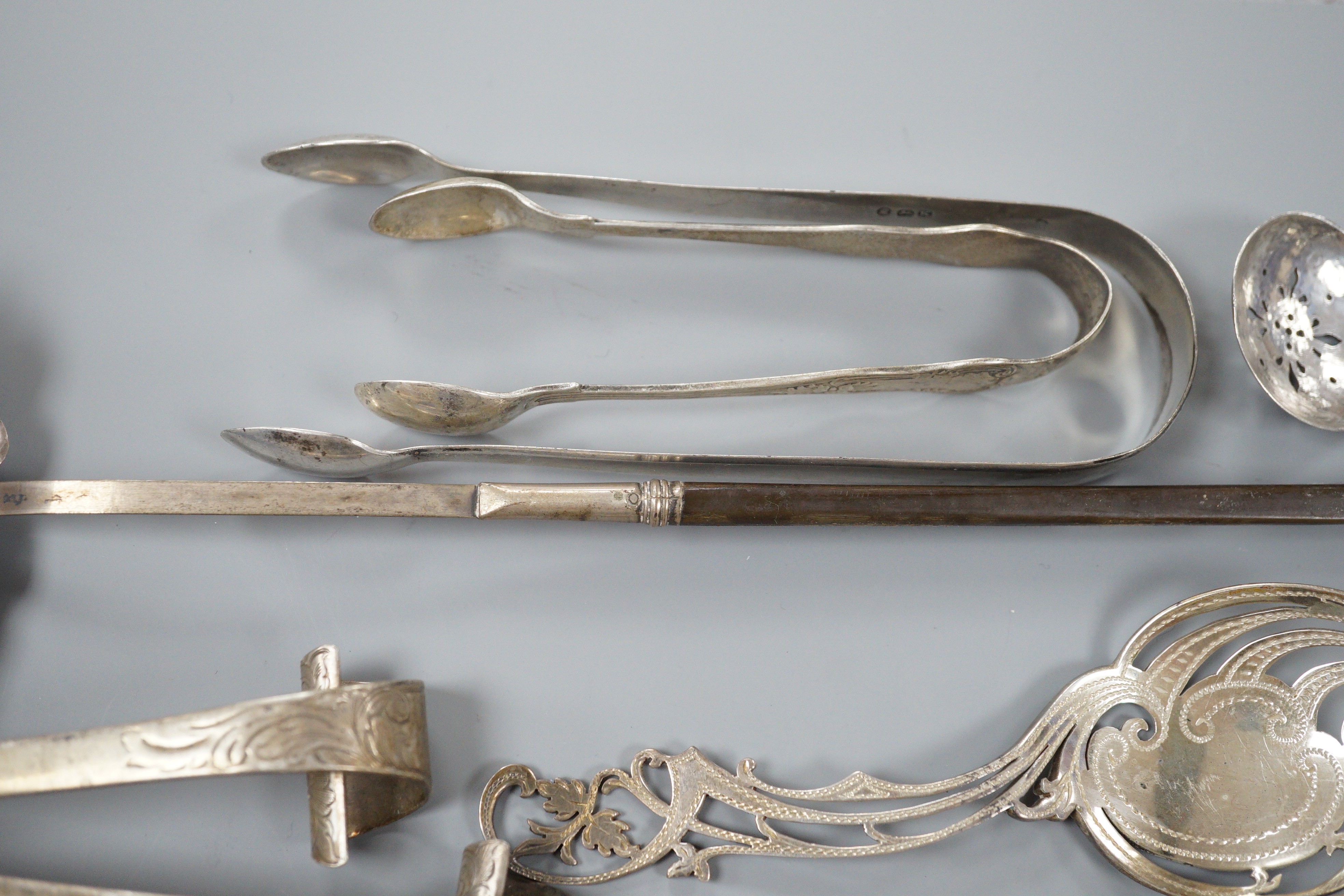 A pair of Victorian silver scrolling knife rests, George Adams, London, 1859, 10.4cm, a pair of pierced silver spoons, two pairs of silver sugar tongs, a part set of Victorian silver dessert eaters(6 & 5), a toddy ladle
